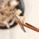 筷子夾著焦脆干貝與小魚乾，背景模糊的零食碟裝滿小魚乾.