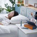 寧靜森林睡眠噴霧瓶身與藍橙色禮盒擺放於臥室白色床頭櫃上，背後有安睡女性和綠色植物.