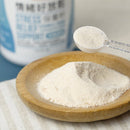 淺米色細緻保養粉裝於木質小盤，透明量匙盛取粉末，背景模糊產品包裝標籤文字.