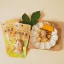 南瓜燒雞包裝兩包擺放，旁邊餐盤內有燒雞塊與南瓜片，背景綠葉點綴.