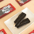 白色方形盤上兩支黑色關東煮烘乾零食串，背景紅色包裝袋散落四周.