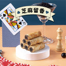 黑芝麻餡法國奶油蛋捲五入堆疊擺放，背景有撲克牌和黑芝麻碎粒飾品.
