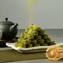 京都宇治抹茶蛋捲堆疊在白色陶盤上，背景有黑色茶壺與茶筅.