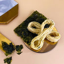 日式海苔蛋捲擺放在鏡面金屬盤上，旁邊有完整及碎裂的海苔片，背景淺米色.
