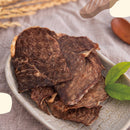 原味牛肉乾片，深褐色質地，擺放於淺灰色陶瓷盤上，旁有綠葉裝飾.