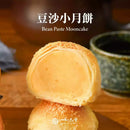 金黃酥皮豆沙小月餅半切展示，背景模糊杯子與木質桌面.