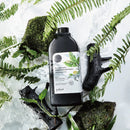 黑色瓶身三合一沁涼茶樹洗髮沐浴露，1000ml，擺放於冰塊與綠葉間.