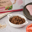白瓷碗盛放深棕色低敏狗飼料，旁邊擺有新鮮番茄切片與生雞胸肉片.